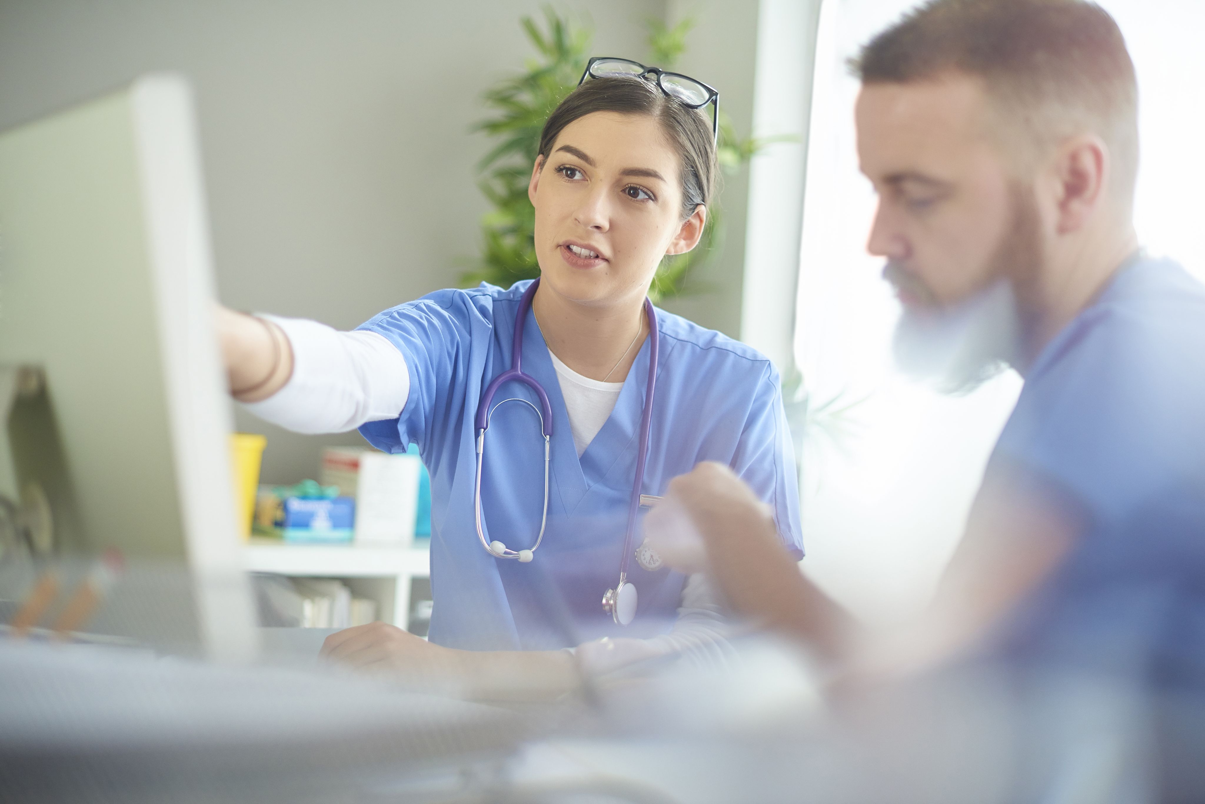 Two NHS workers talking by a computer
