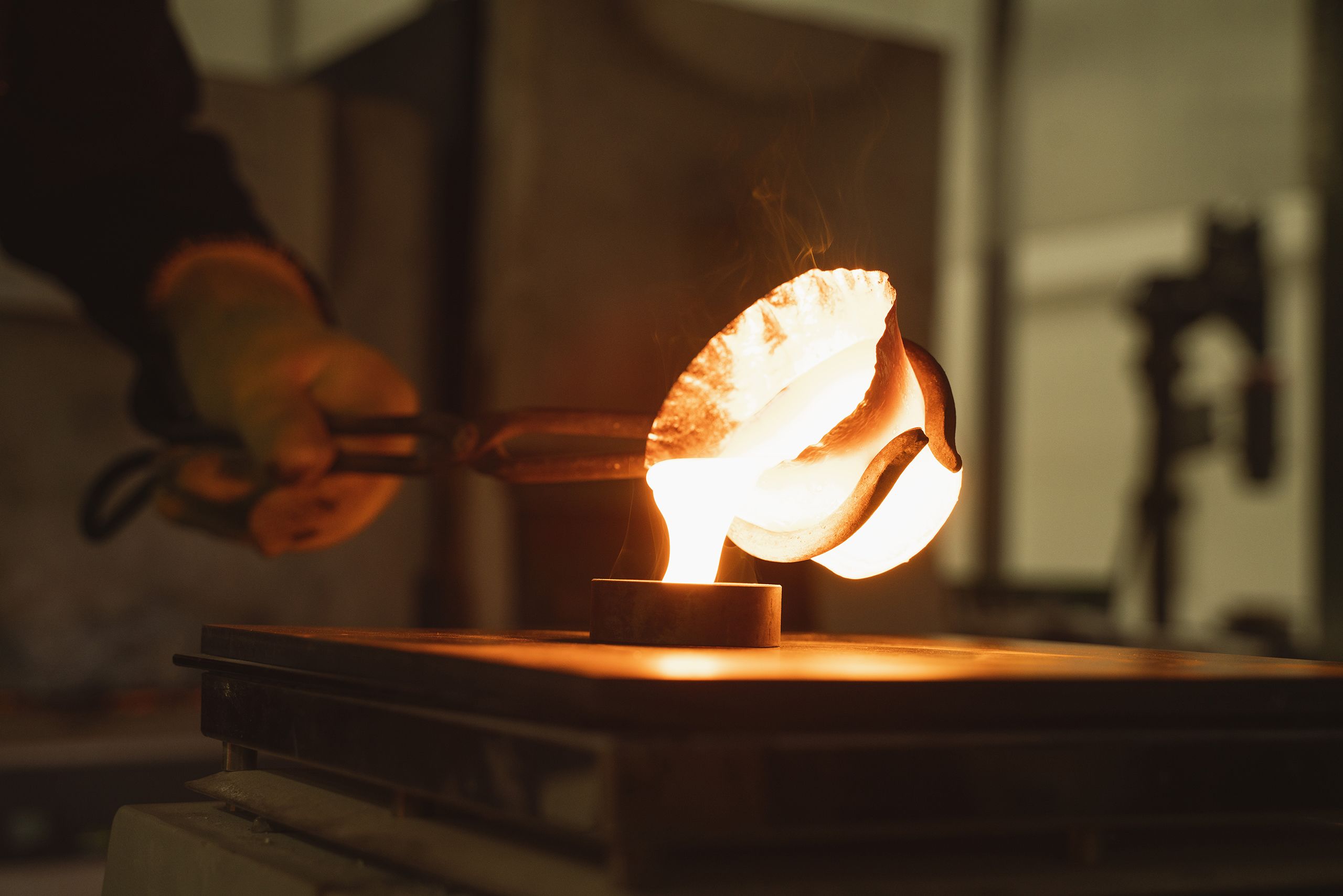 Researcher pouring liquid glass from a crucible into a mould using long tongs and wearing thermal gloves