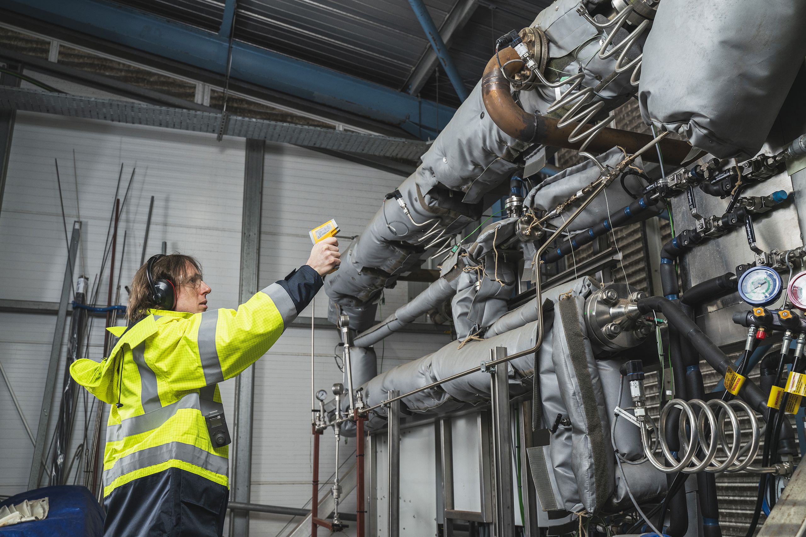 Researcher wearing a high visibility jacket using a pyrometer to measure the temperature of industrial equipment