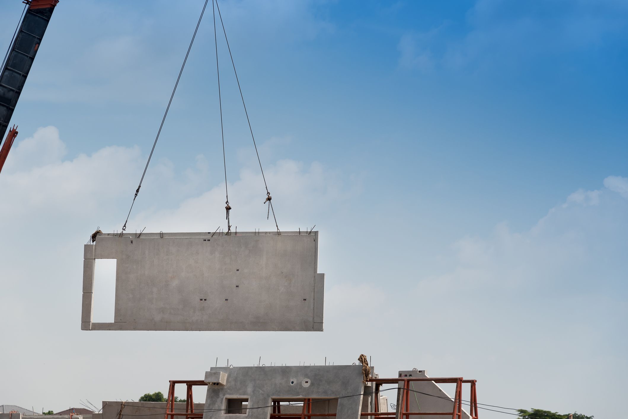Construction site crane is lifting a precast concrete wall panel to installation building