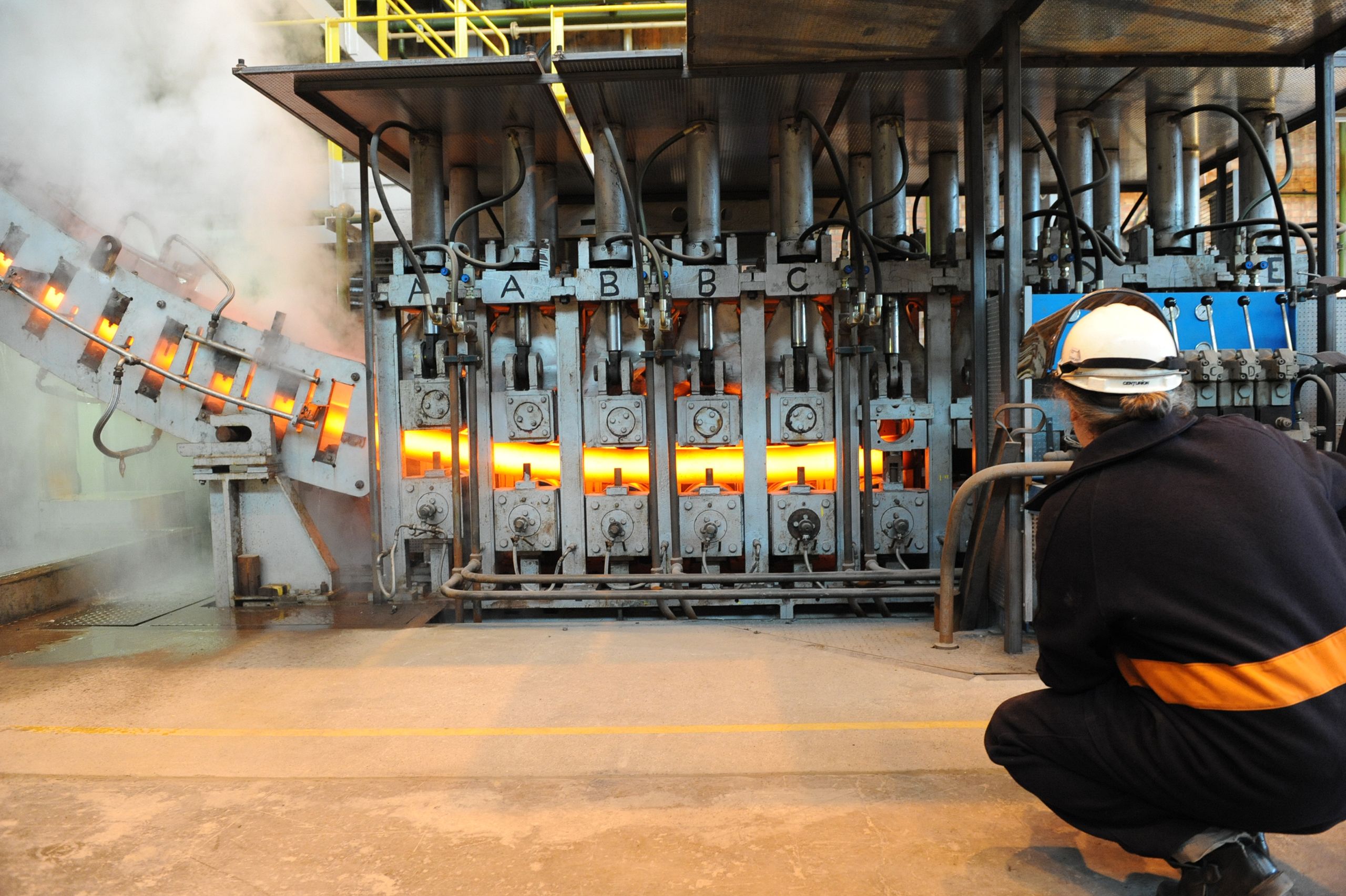 Researcher watching semi-solid steel pass through a rolling mill causing the release of steam