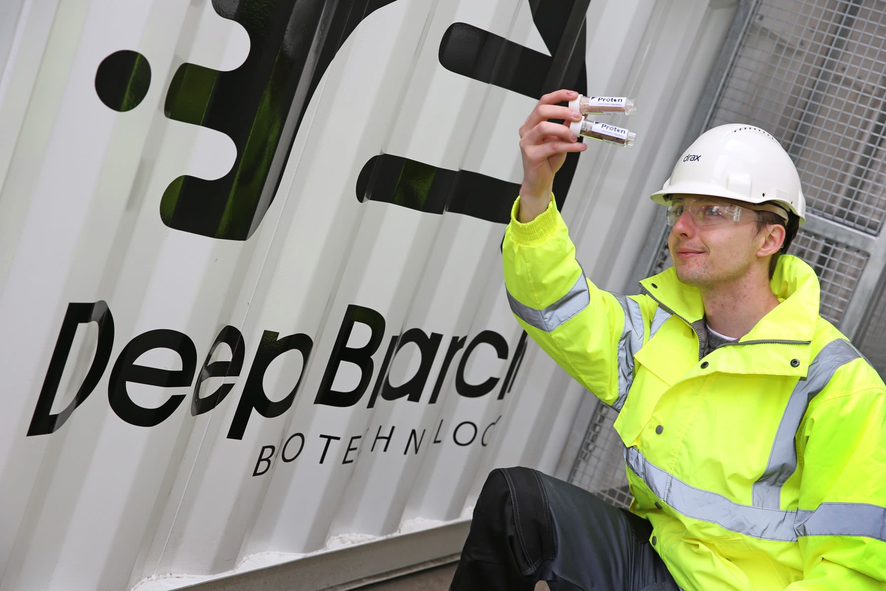 Scientist holding two test tubes next to Deep Branch container unit 
