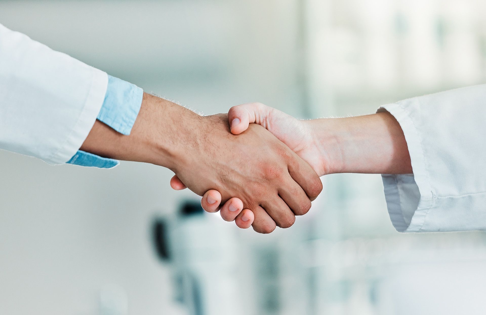 A closeup image of two scientists in laboratory coats shaking hands. 