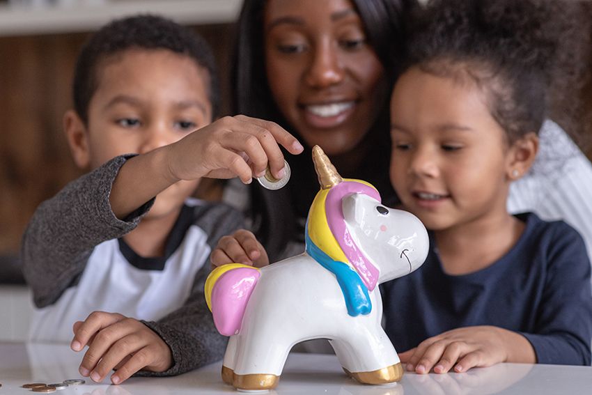A mother teaches her two children the importance of saving money, children shown adding pocket money to the unicorn shape money box.