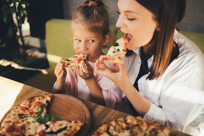 A mother and daughter eat pizza in a cafe.