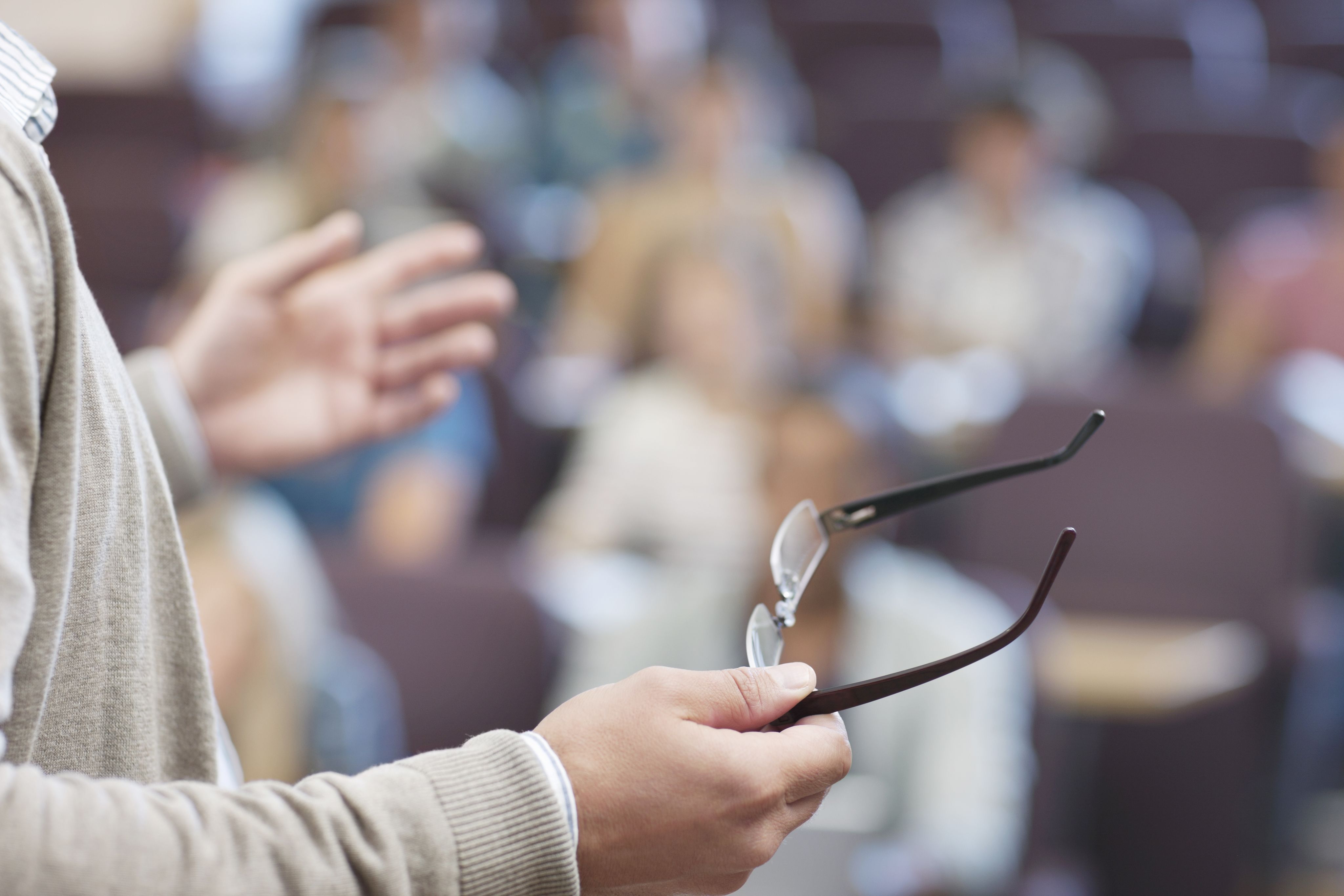 Professor holding eyeglasses and gesturing in a seminar