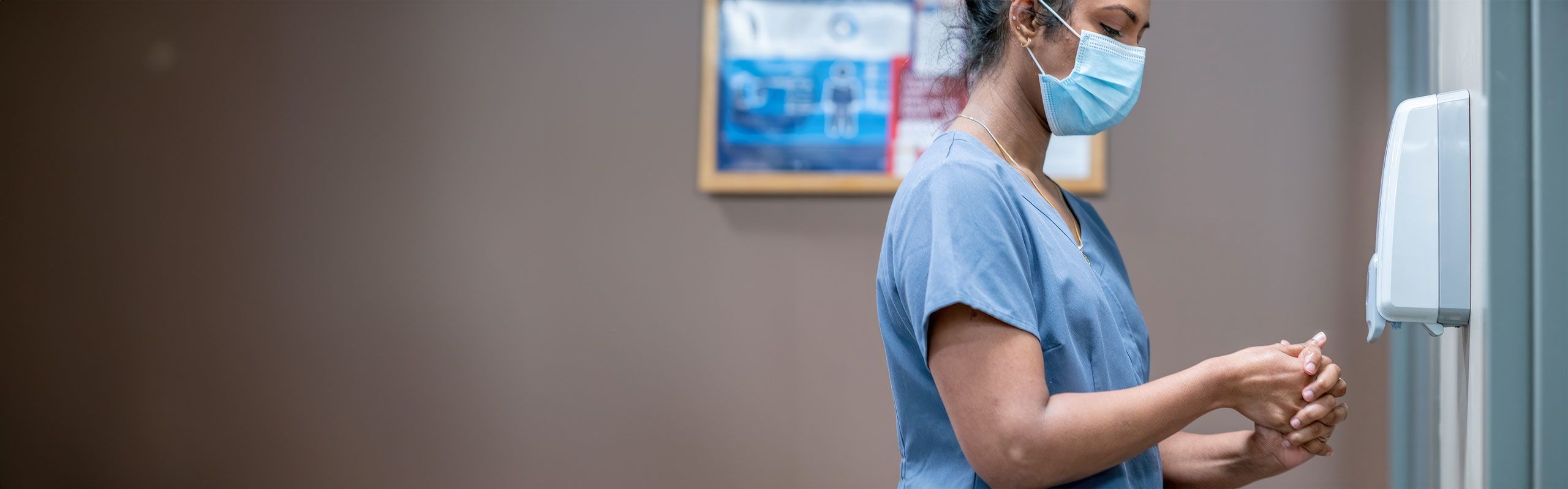 A woman in a medical face mask and scrubs washing her hands