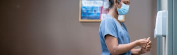A woman in a medical face mask and scrubs washing her hands