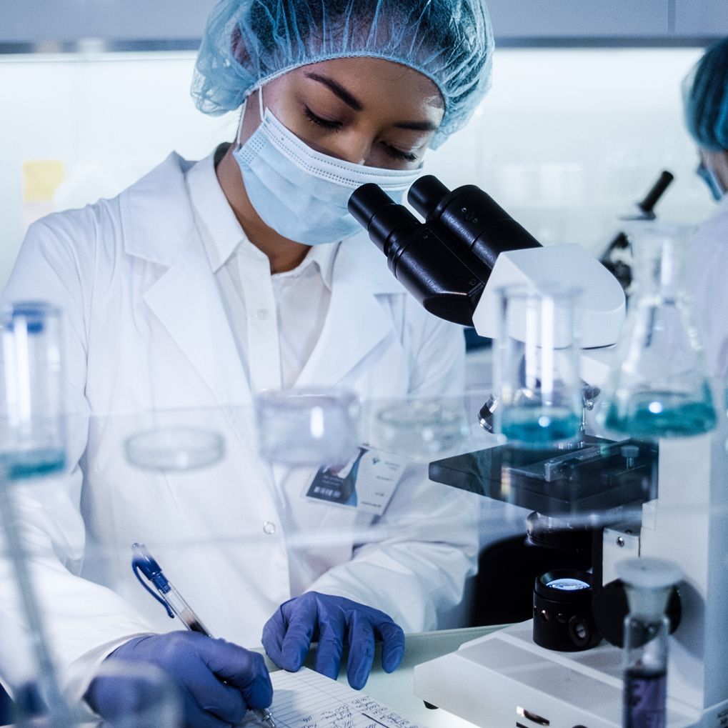 A scientist writing notes in a lab with microscopes