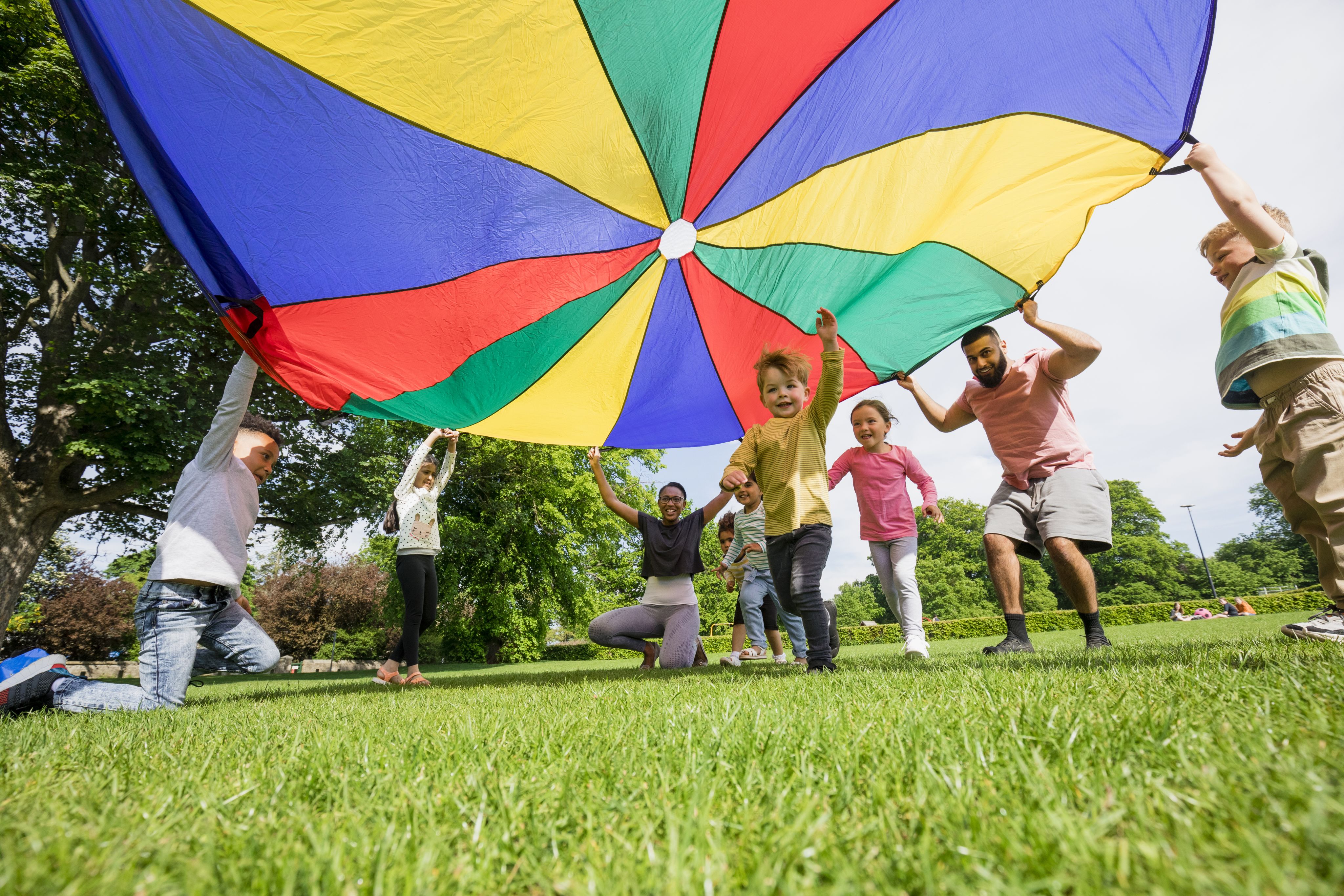 Children and teachers play outside under a coloured canopy