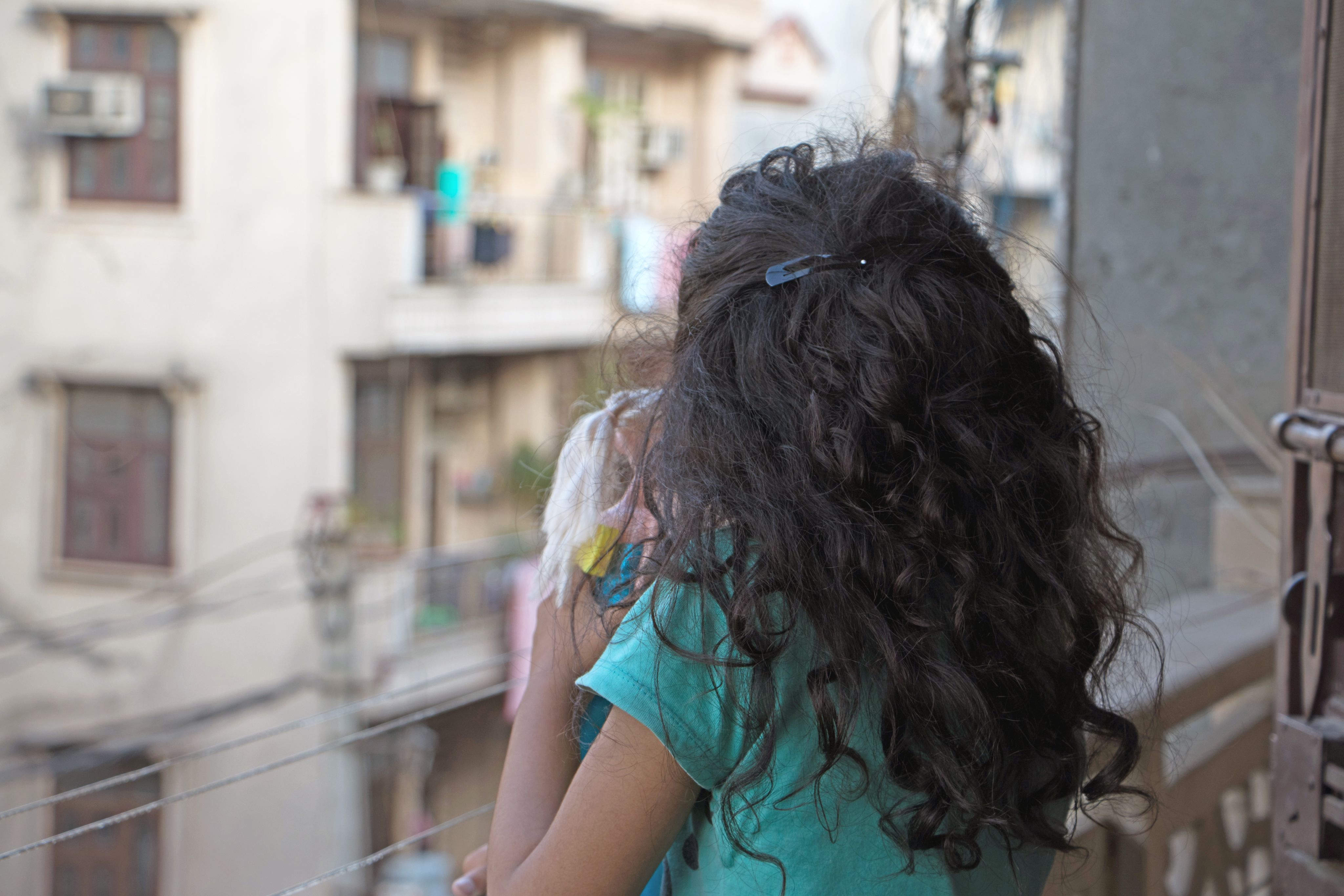 A young girl holding a doll looks down from a balcony