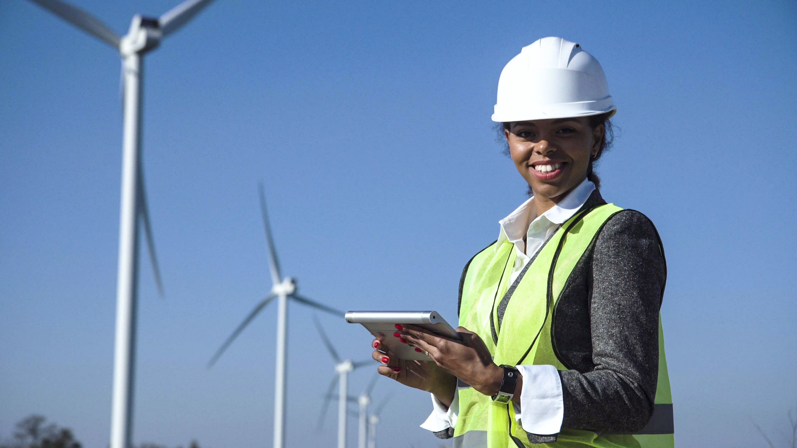 woman working on an iPad in a helmet amongst wind turbines
