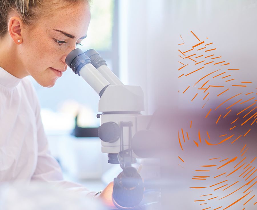 A woman wearing a white lab coat looks into a microscope