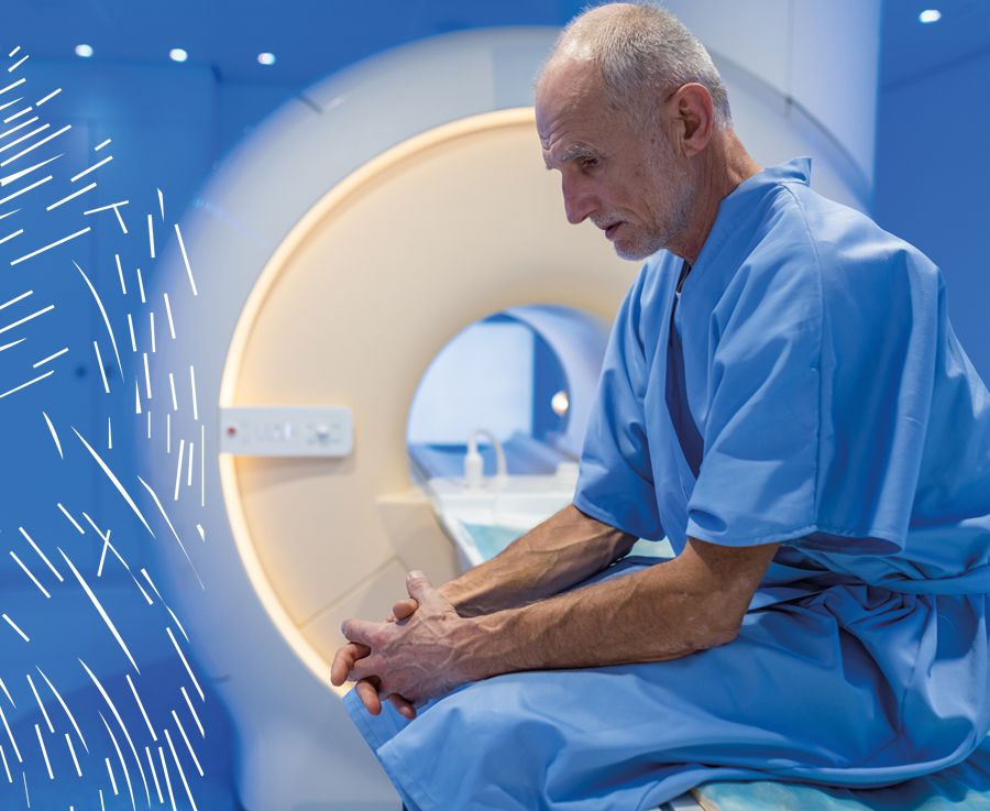 An older man wearing a blue hospital gown sits in front of an MRI scanning machine
