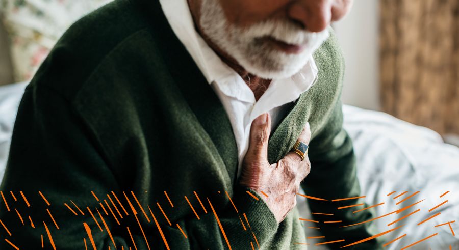 A man in his 60s sat on a bed clutching his chest