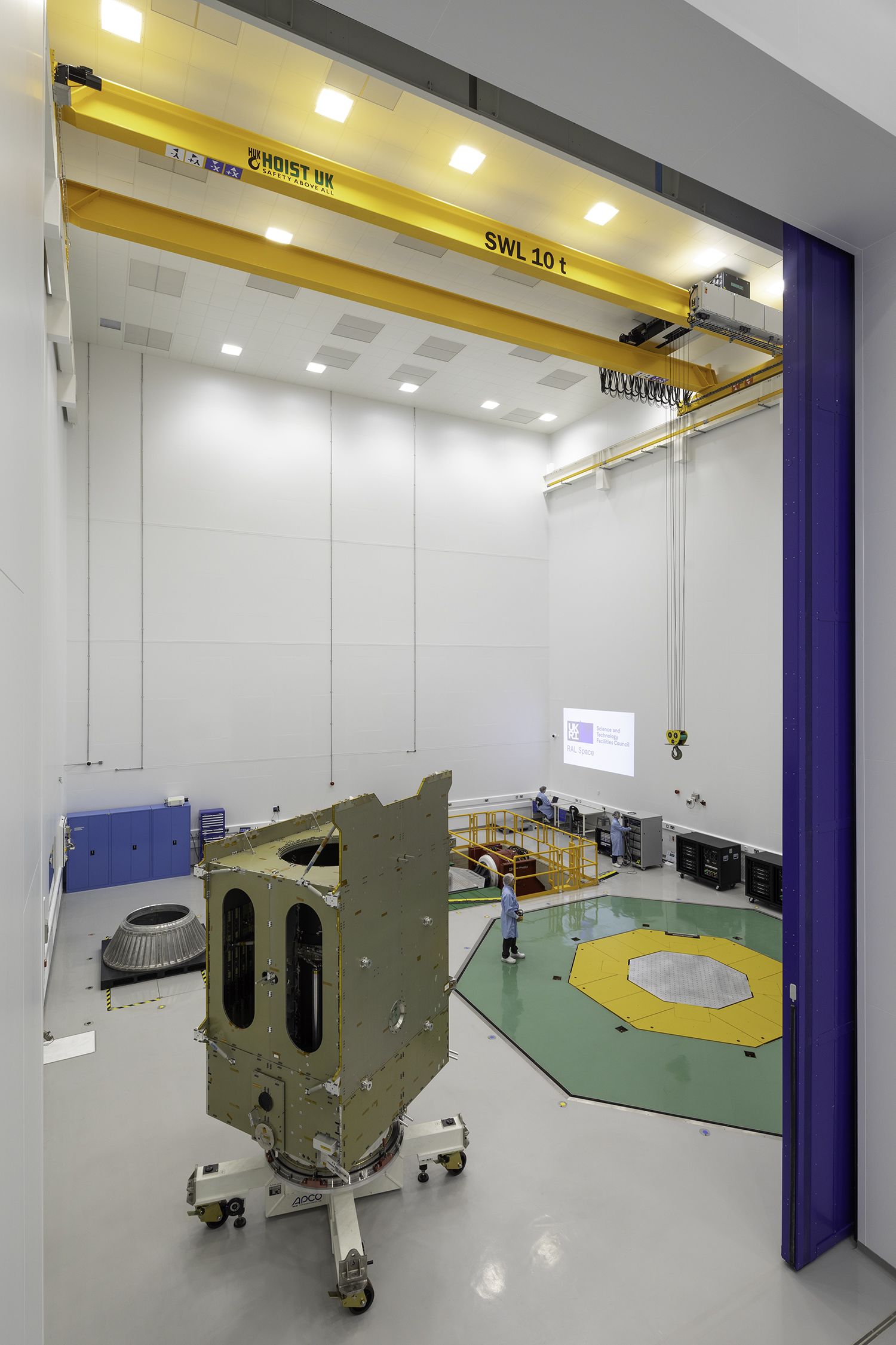 A very tall room with two shaker tables embedded into the floor, and a large satellite model.