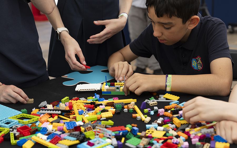 Three school students building a satellite structure from Lego. There are lots of colourful Lego bricks across the table.