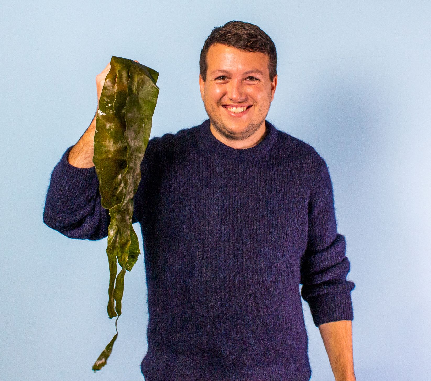 Pierre Paslier, smiling holding up in his right hand, a sample of the seaweed, Notpla products are derived from.
